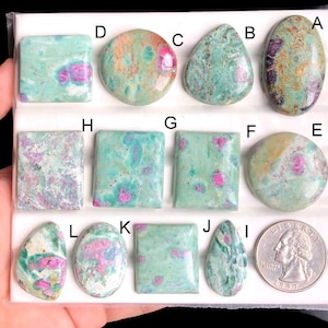 Könnte beinhalten: Eine Sammlung von Rubinen in Zoisit-Edelsteinen in verschiedenen Formen. Die Edelsteine weisen eine Mischung aus Formen auf, darunter oval, tropfenförmig und quadratisch. Die Farben sind eine Mischung aus Grün und Rosa. Eine Münze ist zum Größenvergleich enthalten.