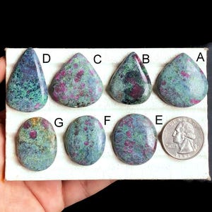May include: Assortment of seven green, blue, and pink ruby zoisite cabochons in various shapes and sizes, labeled A through G. A US quarter is included for scale.