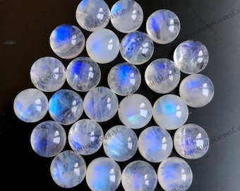 Op de afbeelding: Een verzameling van 18 ronde, witte maansteen cabochons met iriserende blauwe flitsen. De cabochons zijn ongeveer 10 mm in diameter en zijn perfect voor het maken van sieraden.