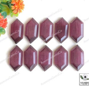 May include: A collection of ten faceted, elongated, hexagonal gemstones in a deep reddish-purple hue. The gemstones are arranged in a grid pattern, showcasing their polished surfaces and geometric shapes. The background is white.
