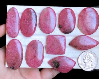May include: Assortment of ten pink and white rhodochrosite cabochons in various shapes and sizes, displayed on a white foam board.