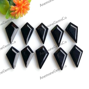 May include: A collection of ten black gemstone kite-shaped cabochons. The gemstones are arranged in two rows, with a bright white background. The gemstones are polished and reflect light.