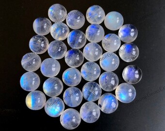 Op de afbeelding: Een verzameling van 25 ronde, witte maansteen cabochons met iriserende blauwe en gele flitsen. De stenen zijn glad en gepolijst en liggen los in een hoop.