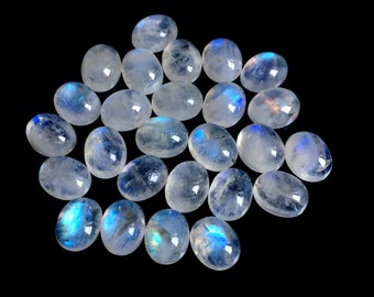 May include: A collection of oval-shaped moonstone gemstones. The stones are translucent with a milky white base and exhibit a blue adularescence. The gemstones are displayed against a black background.
