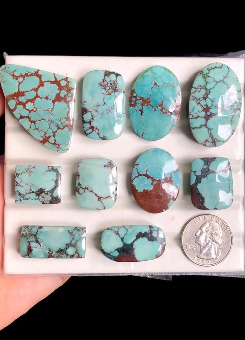May include: A collection of turquoise gemstones in various shapes, including oval, rectangular, and freeform. The stones feature a striking blue-green color with brown matrix patterns. A US quarter is included for size reference.