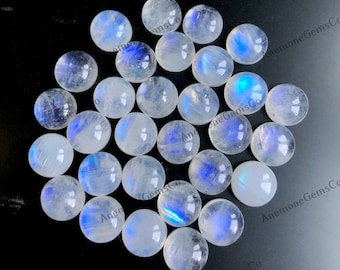 Op de afbeelding: Een verzameling van 20 ronde, witte maansteen cabochons met iriserende blauwe flitsen. De cabochons zijn ongeveer 10 mm in diameter.