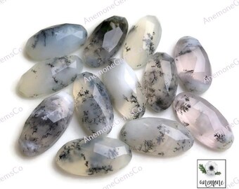 Op de afbeelding: Een verzameling van twaalf ovale, doorschijnende, witte agaat cabochons met dendritische insluitsels. De stenen hebben een natuurlijke, bewolkte en gevlekte uitstraling.