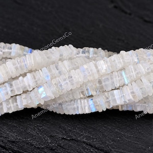 Puede incluir: Un hilo de cuentas de piedra lunar translúcidas de color blanco roto con forma de discos planos y finos. Las cuentas muestran un sutil destello azul iridiscente en sus superficies. El texto AnemoneGemsCo es visible al fondo y un logo.