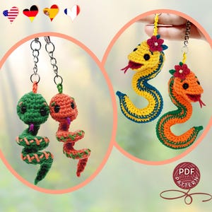 Pode incluir: Chaveiros de cobra de crochê em verde, laranja e amarelo com detalhes vermelhos. As cobras têm olhos pretos e línguas rosas. Um chaveiro apresenta uma cobra amarela com listras azuis e uma flor vermelha. O outro tem uma cobra laranja com listras verdes e uma flor vermelha.