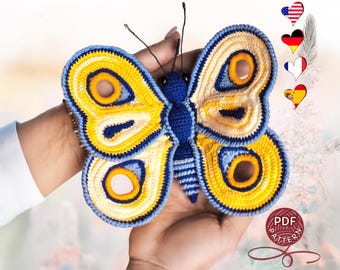 May include: A crocheted butterfly amigurumi toy with blue and yellow wings. The butterfly has a blue body and a yellow and white pattern on its wings. The toy is held in a person's hand.