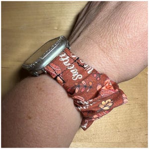 May include: A brown and orange patterned watch band with the text "Life is Sweet" on it. The band is worn on a wrist.