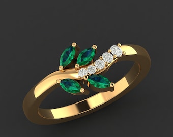 May include: A gold ring featuring a leaf design with marquise-cut emeralds and round diamonds. The ring has a polished finish and is set against a dark background. The gemstones are arranged in a delicate, nature-inspired pattern.