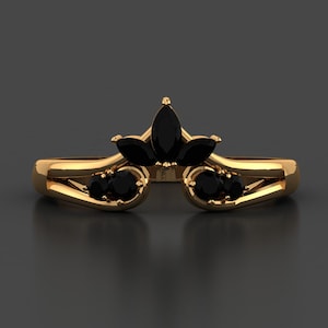 May include: A gold-colored ring with a unique design. The ring features a central cluster of black gemstones in a floral arrangement, with additional black gemstones set on either side. The band has a split design.