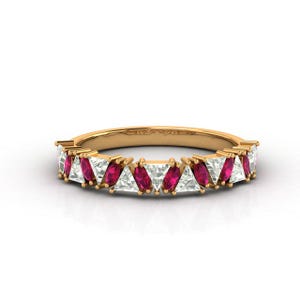 May include: A gold band ring with alternating triangular and marquise-cut gemstones. The ring displays vibrant red and clear white stones, creating a striking contrast. The gemstones are set closely together, forming a continuous pattern around the band.