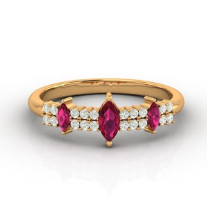 以下が含まれることがあります： 3つのマーキス型ルビー色の宝石をあしらったゴールドリング。小さな丸い白い宝石で装飾されています。ゴールドバンドにセットされたリングです。