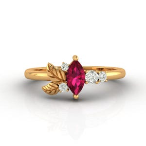 Puede incluir: Anillo de oro con un rubí central en forma de marquesa y tres pequeños diamantes blancos. El anillo tiene un diseño de hojas. La banda es de oro pulido.