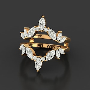 Könnte beinhalten: Ein goldfarbener Ringschutz mit weißen Edelsteinen im Marquise- und Rundschliff. Der Ringschutz hat ein Doppelband-Design, wobei die Edelsteine in einem floralen Muster angeordnet sind. Der Ring ist vor einem dunklen Hintergrund platziert.