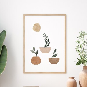 May include: A framed print with a minimalist design featuring three abstract pots with green plants and a brown circle in the top left corner. The print is hanging on a white wall above a wooden console table with a rattan chair and a vase with green branches.