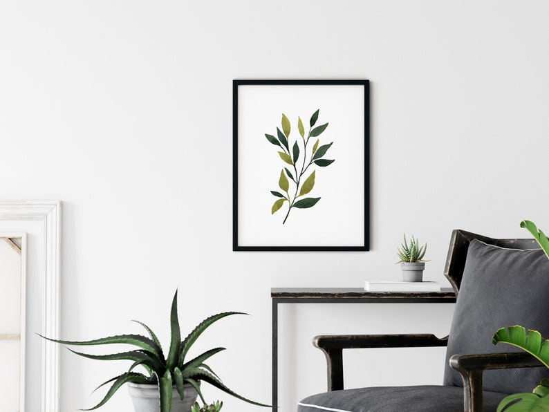 Op de afbeelding: Een zwart ingelijst afdruk van een aquarel van een groene en gele bladertak op een witte achtergrond.