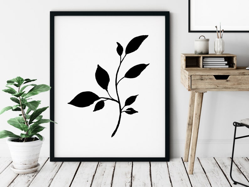 Pode incluir: Impress&atilde;o art&iacute;stica minimalista em preto e branco com uma silhueta estilizada de um ramo com folhas. A impress&atilde;o &eacute; emoldurada em uma moldura preta e exibida em uma parede branca.