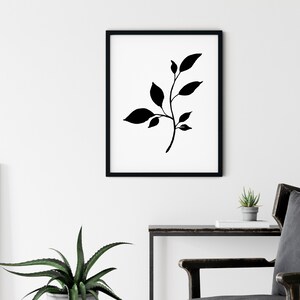 Pode incluir: Impress&atilde;o minimalista em preto e branco com uma silhueta estilizada de um ramo frondoso com folhas delicadas. A impress&atilde;o &eacute; emoldurada em uma moldura preta e pendurada em uma parede branca.