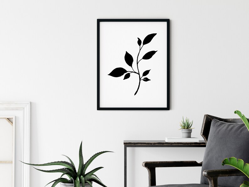 Pode incluir: Impress&atilde;o minimalista em preto e branco com uma silhueta estilizada de um ramo frondoso com folhas delicadas. A impress&atilde;o &eacute; emoldurada em uma moldura preta e pendurada em uma parede branca.