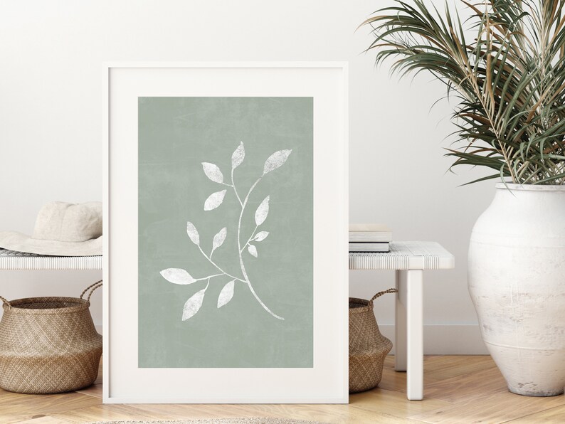 May include: A framed print featuring a white branch with leaves against a sage green background.
