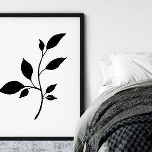 Pode incluir: Impress&atilde;o minimalista em preto e branco de um ramo estilizado com folhas. A impress&atilde;o est&aacute; emoldurada em uma moldura preta e pendurada em uma parede branca.
