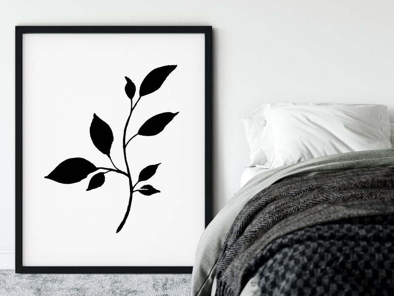 Pode incluir: Impress&atilde;o minimalista em preto e branco de um ramo estilizado com folhas. A impress&atilde;o est&aacute; emoldurada em uma moldura preta e pendurada em uma parede branca.