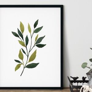 Op de afbeelding: Een aquarel schilderij van een tak met groene en gele bladeren. De tak is afgebeeld in een minimalistische stijl, met een witte achtergrond.