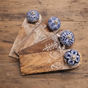 May include: Four wooden doorstops with decorative blue and white ceramic knobs. The doorstops have a light brown finish with white painted designs. The knobs have a floral pattern and silver hardware.