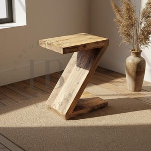 May include: A Z-shaped side table crafted from light brown wood with a visible natural grain pattern. The table features a flat rectangular top, a diagonal support section, and a flat rectangular base, creating a continuous angular silhouette.