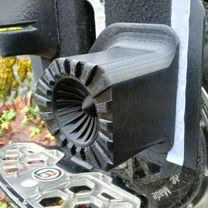 Peut inclure: Gros plan d'un composant noir imprimé en 3D, fixé à un véhicule électrique personnel. Le composant présente un design en forme de turbine avec une série de pales. Le repose-pieds est argenté avec un motif en nid d'abeille.