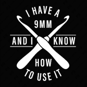 May include: Black graphic with white text and crossed crochet hooks. The text reads "I HAVE A 9MM AND I KNOW HOW TO USE IT". The design is a humorous statement for crocheters.