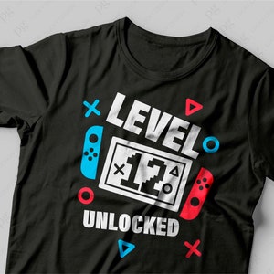 K&ouml;nnte beinhalten: Schwarzes T-Shirt mit einer wei&szlig;en Grafik, auf der "Level 12 Unlocked" mit einem Videospiel-Controller-Design steht.