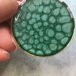 Peut inclure: Un pendentif rond avec un motif marbré vert et bleu. Le pendentif est serti dans une bélière argentée avec un bord doré.