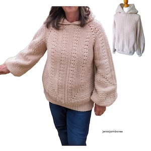 May include: A beige crocheted hooded sweater with a loose fit and a textured stitch pattern. The sweater has long sleeves and a relaxed, oversized style.