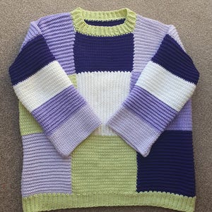 May include: A long-sleeve crochet jumper featuring a colour-blocked patchwork design. The garment is constructed from rectangular panels in shades of lime green, lavender, white, and deep navy blue, finished with a lime green ribbed neckline.