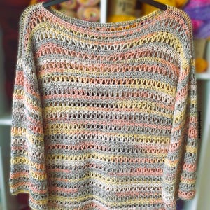 Op de afbeelding: Een handgemaakte, opengebreide gehaakte trui in een spectrum van kleuren, waaronder perzik, geel, grijs en crème. De trui heeft een ronde halslijn en lange mouwen. Het garen lijkt een zacht, lichtgewicht materiaal te zijn, perfect om te dragen.
