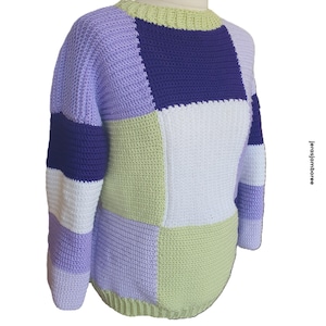 Könnte beinhalten: Ein gehäkelter Pullover mit Patchwork-Muster in den Farben Lila, Grün und Weiß.