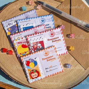 May include: A set of five colorful sticker sheets with different designs. The sticker sheets are shaped like envelopes and feature illustrations of a chick, a person with a hat, a red apple, and a balloon. The sticker sheets have the text "Deepspace Delivery Sticker Set" printed on them.