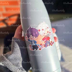May include: A light gray water bottle with a sticker featuring two cartoon characters. One character has purple hair and the other has white hair. The sticker has a floral design and musical notes.