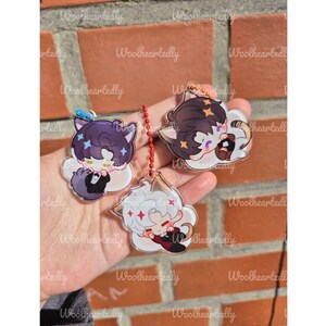 Pode incluir: Tr&ecirc;s pingentes de acr&iacute;lico transparente com personagens estilizados de anime com orelhas de gato. Um personagem tem cabelo escuro, um tem cabelo claro e um tem cabelo escuro com um la&ccedil;o azul. Cada pingente est&aacute; preso a uma corrente de bolinhas vermelha.