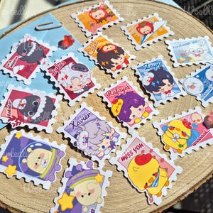 May include: A set of 15 colorful stickers featuring various cartoon characters and designs. The stickers are shaped like postage stamps and have a scalloped edge. Some of the characters include a penguin, a chick, a bunny, and a person with purple hair. The stickers have text on them, including "Caleb", "Sylus", "Zayne", "Rafayel", "Xavier", "to-doaa", "Waaaaak", "miss you", and "Calala".