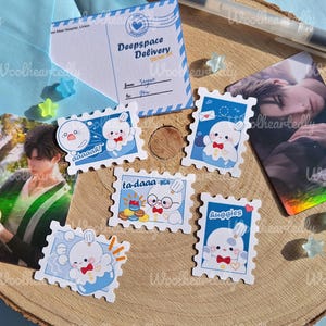 May include: A set of ten colorful stickers featuring cartoon characters with different expressions. The stickers are shaped like postage stamps and have a blue background with white borders. The text on the stickers includes "Deep Space Delivery", "ta-daaa", "aww-aaah", "Huggies", and "From: Faye To: You".