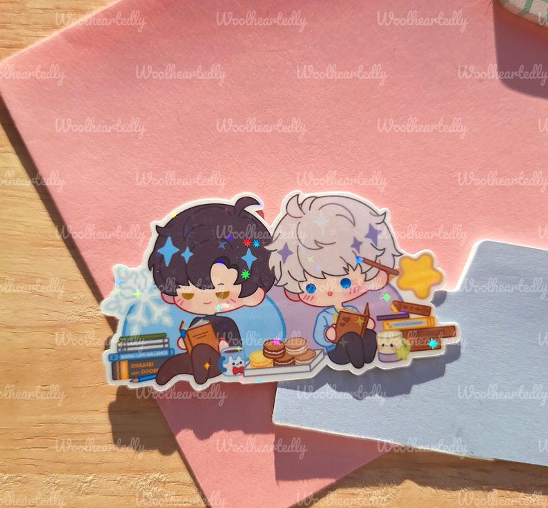 May include: A sticker featuring two anime-style characters, one with dark hair and the other with light hair, both reading books. The sticker includes stacks of books, pastries, and a star-shaped wand. The background is a pink and blue surface.