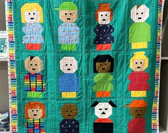 Puede incluir: Una colcha verde con un borde colorido presenta 12 personajes diferentes, incluyendo personas, animales y un perro. Los personajes están hechos de cuadrados de tela de diferentes colores y están dispuestos en una cuadrícula.