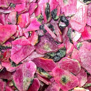 Puede incluir: Una vista cercana de un montón de piedras preciosas de rubí rosa. Las piedras en bruto sin cortar tienen una variedad de formas y tamaños, algunas mostrando un tono verde.