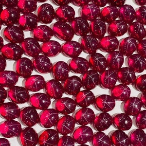 May include: A collection of oval-shaped, red star ruby cabochons. The stones have a deep red color and a star-like pattern.