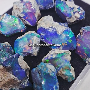 May include: A collection of raw opal gemstones. The opals display vibrant blue, green, and purple iridescence, with rough, gray matrix. The text "KingLabradoriteGems" is visible. These gemstones are ideal for jewelry making or collecting.
